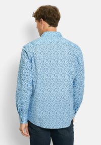Hellblaues Button-up-Hemd mit floralem Muster in dunklerem Blau. Lange Ärmel mit geknöpften Manschetten, klassischer Kragen und abgerundeter Saum.