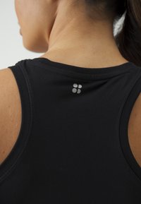 Čierny atletický top bez rukávov s okrúhlym výstrihom a širokými prieramkami. Na hornej časti chrbta sa nachádza malé strieborné logo. Hladká, elastická látka.