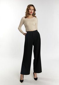 Beiger gerippter Crop-Top mit dezenten Verzierungen, kombiniert mit hochgeschnittener, weiter schwarzer Hose und schwarzen spitzen Pumps.