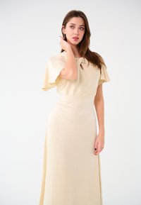 Helles beige Maxikleid mit kurzen, schwingenden Ärmeln, einem Schlüssellochausschnitt, glatter Textur und einer taillierten Taille, die in einen fließenden Rock übergeht.