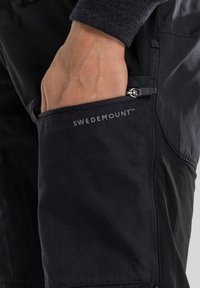 Black hiking pants with a zippered pocket. Features "SWEDEMOUNT™" logo. Material appears durable and textured, designed for outdoor use.