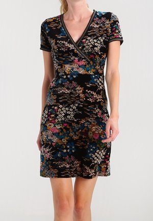 Woman wearing a short-sleeve, knee-length black dress with a colorful floral pattern and a V-neck wrap style.