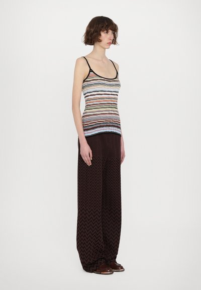 Striped tank top in multicolor patterns with black trim, paired with wide-leg brown pants featuring a zigzag design. Brown footwear completes the look.