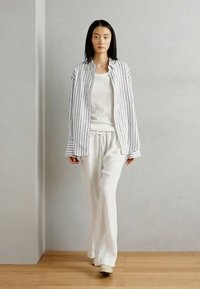 Chemise à rayures, à boutonnières, en blanc et gris, associée à un pantalon blanc ample. Tissu doux avec une silhouette décontractée.