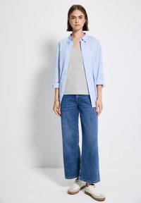 Camicia azzurra chiara a maniche lunghe, canotta grigia, jeans a gamba larga blu e sneakers bianche con dettagli color sabbia. Design semplice, vestibilità casual e materiali morbidi.