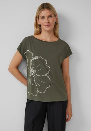 T-shirt vert olive à manches courtes, arborant un grand motif floral argenté en sequins sur le devant. Matière en coton doux.