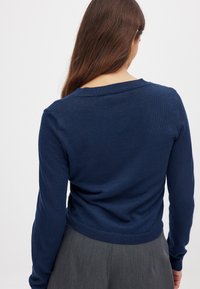 Dunkelblaues Strickpullover mit rundem Halsausschnitt und gerippten Bündchen. Hat eine figurbetonte Silhouette und glatte Textur, von hinten gesehen.