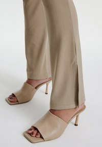 Beige open-toe muiltjes met een vierkante neus, gemaakt van soepel leer, hebben een slanke hoge hak en worden gecombineerd met lichtbeige geribde broeken met splitten.