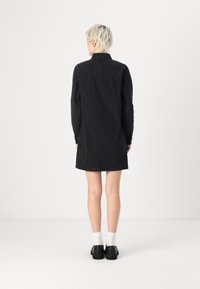 Black denim shirt dress with a collar, long sleeves, and a straight cut. Features buttoned cuffs and a rounded hem.