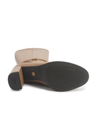Bota beige hasta la rodilla con puntera redondeada, parte superior sintética lisa, tacón cuadrado, suela de goma y acento metálico cerca de la cremallera.