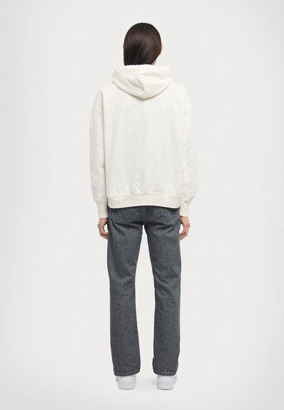 White hoodie with a drawstring, ribbed cuffs, and hem, paired with dark gray straight-leg jeans and white sneakers. View from the back.