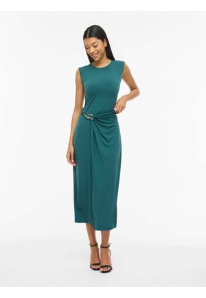 Vrouw lacht, draagt een mouwloze teal midi-jurk met een knoopdetail aan de zijkant en zwarte enkelriem hakken, staat op een witte achtergrond.