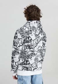Felpa con cappuccio di base bianca, coperta da testo e motivi in stile graffiti neri. Presenta maniche lunghe e orlo a coste.