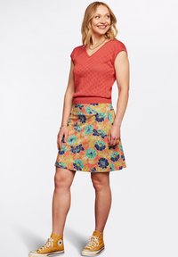 Czerwona, krótkoszeregowa, dzianinowa bluzka z wzorem serc; pomarańczowa spódnica w kwiaty z niebieskimi i zielonymi akcentami; żółte trampki za kostkę.