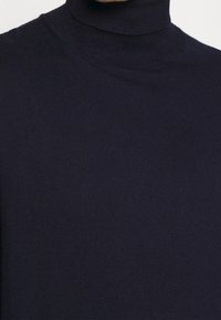 Maglione a collo alto in maglia blu navy con una texture liscia e un design aderente, dotato di un alto colletto e dettagli a costine sui bordi.