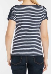 Marineblau-weiß gestreiftes T-Shirt mit kurzen Ärmeln, das über eine strukturierte Schulterpartie und einen gewellten Saum verfügt. Getragen mit dunklen Jeans.