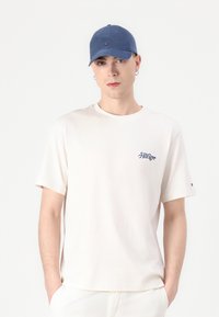 Kremna kratka majica s kratkimi rokavi z mornarsko modrim logotipom "Hilfiger" na prsih. Modra kapa z detajlom logotipa. Model ima kratke lase in uhane.