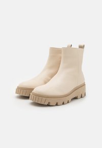Bottes chelsea en cuir beige avec une plateforme épaisse et une semelle crantée. Elles présentent une texture lisse et des languettes pour un enfilage facile.