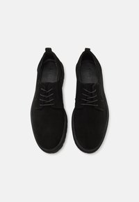 Černé semišové boty s kulatou špičkou, vybavené plochými tkaničkami a texturovanou gumovou podešví. Jednoduchý design s minimem akcentů.