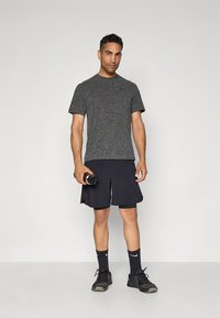 Hall hall sportlik t-särk, mustad lühikesed püksid, hoiab veepudelit. Mustad spordijalatsid ja sokid. Lihtne, funktsionaalne disain, lahtise istuvusega.