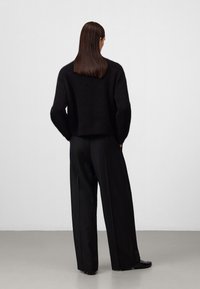 Schwarzer Strickpullover mit lässigem Schnitt und überschnittenen Schultern, kombiniert mit weiten schwarzen Hosen, die einen weichen, strukturierten Stoff zeigen.