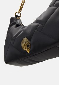 Czarna pikowana torebka o trójkątnym kształcie, z emblematem złotego ptaka i łańcuszkiem jako rączką. Gładka faktura z zamkiem błyskawicznym.