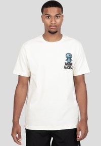 Camiseta de algodón blanca con un personaje de dibujos animados azul y detalles bordados en el lado izquierdo del pecho, complementada por un texto negro en negrita debajo.