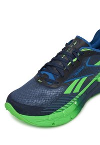 Scarpe da atletica blu e verdi con parte superiore testurizzata, dettagli riflettenti e suola spessa con design di battistrada scanalato. Lacci neri e logo.