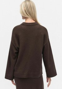 Bruine gebreide trui met een boxy pasvorm, verlaagde schouders, ribbelkraag en boorden. Soepele textuur, gemiddelde dikte en minimale details.