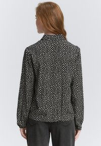 Chemise noire à manches longues avec un motif taché blanc, design à col, et manches froncées, associée à un pantalon taille haute sombre.
