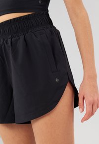 Zwarte sportshorts met een elastische tailleband, zijzakken en een afgeronde zoom. Gemaakt van lichtgewicht stof met een subtiel logodetail.