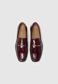 Burgunderfarvede loafers med en skinnende patenteret finish, firkantet tå, guldtonet accent over oversiden og en sort gummiels.