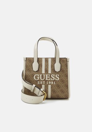 Small brown and beige Guess handbag with logo print, white handles, vertical stripes, and a detachable white shoulder strap with gold buckle.