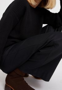 Czarny sweter z prążkowanej dzianiny, w połączeniu z czarnymi spodniami o szerokich nogawkach i brązowymi botkami na obcasie, charakteryzujący się gładką tkaniną i czystymi liniami.