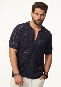 Marineblaues Strickhemd mit einem Netzmuster, kurzen Ärmeln und einem Kragenhalsschnitt, mit Knöpfen auf der Vorderseite. Strukturiertes Design.