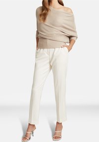 Haut beige en maille côtelée à manches tombantes, associé à un pantalon blanc ajusté. Le haut présente une coupe décontractée et un tissu texturé.