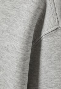 Light gray knitted fabric with visible seam and stitching details, showing texture and folds of a soft garment.
