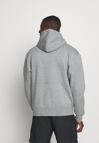 Szara bluza z kapturem o teksturowanym wykończeniu, z dużym kapturem, prążkowanymi mankietami i luźnym krojem. Pokazano widok z tyłu.