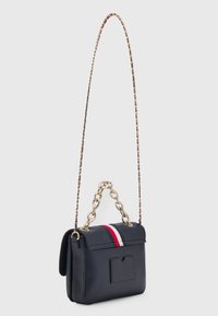 Borsa a tracolla in pelle blu navy con chiusura a patta, tracolla in catena dorata e tasca frontale. Presenta una striscia rossa e bianca sulla patta.