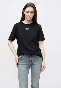 Μαύρο βαμβακερό μπλουζάκι με κοντά μανίκια, με κυκλικό λογότυπο στο κέντρο. Συνδυασμένο με ανοιχτόχρωμο μπλε τζιν παντελόνι.