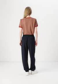 Kortermet topp i rust med mønsterdesign, sammen med marineblå joggebukser med elastisk liv og ribbestrikkede mansjetter. Hvite joggesko.