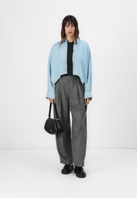 Veste en denim bleu clair coupée, haut noir, pantalon large gris taille haute et sac à main noir avec des accents dorés ; textures lisses.
