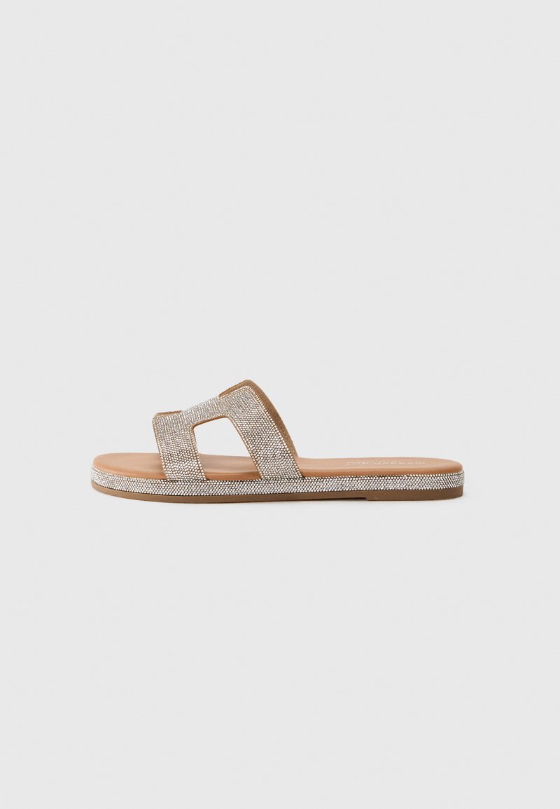 Flat sandal med beige såle, doble stropper dekorert med sølvglitter og en glatt, brun innersåle.