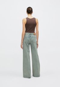 Vaqueros de pierna ancha y talle alto en azul claro con una camiseta de tirantes marrón, que presenta un logotipo en parche en la espalda y una textura suave de algodón.