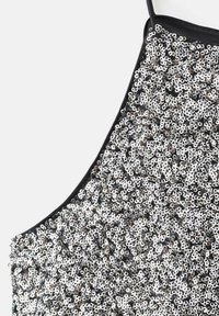 Strieborný tank top posiaty flitrami s čiernym lemovaním, s hustým vzorom lesklých kruhových flitrov, ktorý vytvára textúrovaný povrch.