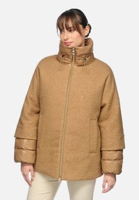 Chaqueta marrón texturizada con cuello alto, cierre de cremallera y mangas abullonadas brillantes en color marrón claro. Presenta un bolsillo en la parte frontal y detalles de costura robustos.