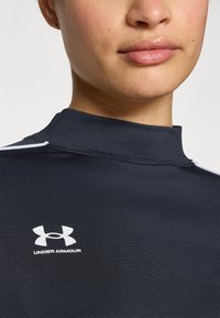Black athletic top with a high collar, featuring a white Under Armour logo on the chest and contrasting white piping on the shoulders.