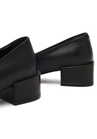 Chaussures noires à talons carrés en cuir lisse avec un design simple. Les talons sont courts, carrés et ont une finition mate.