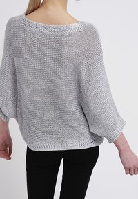 Grauer, übergroßer Strickpullover mit lockerem, offenem Rückendesign und Fledermausärmeln. Strukturierte Webart mit einer entspannten Passform.