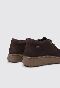 Baskets en cuir marron avec une finition texturée, présentant une semelle à couture contrastée et un petit logo rouge sur le côté. Design basse.